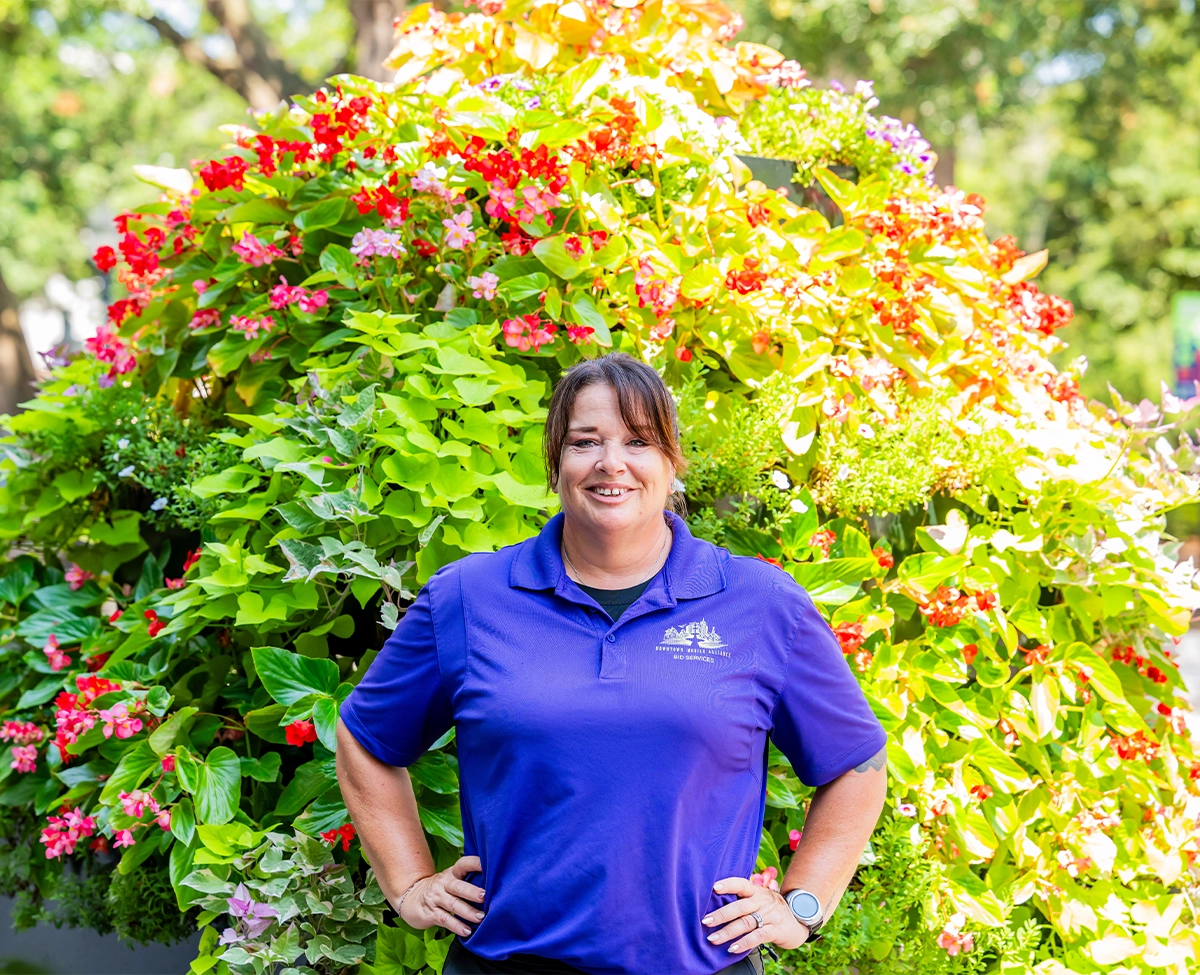 Downtown Mobile Alliance BID Services Ambassador posing in front of tiered flower planter blooming in the spring