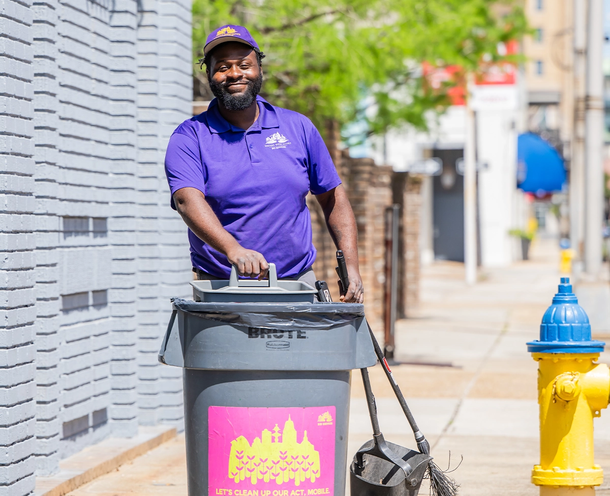 Downtown Mobile Alliance BID Services Ambassador Cleaning streets with broom and rolling trash can